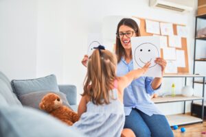 Young therapist woman speaking and treating child, counselor and behaviour correction at pedagogue payroom showing happy and sad faces Young therapist woman speaking and treating child, counselor and behaviour correction at pedagogue payroom showing happy and sad faces
