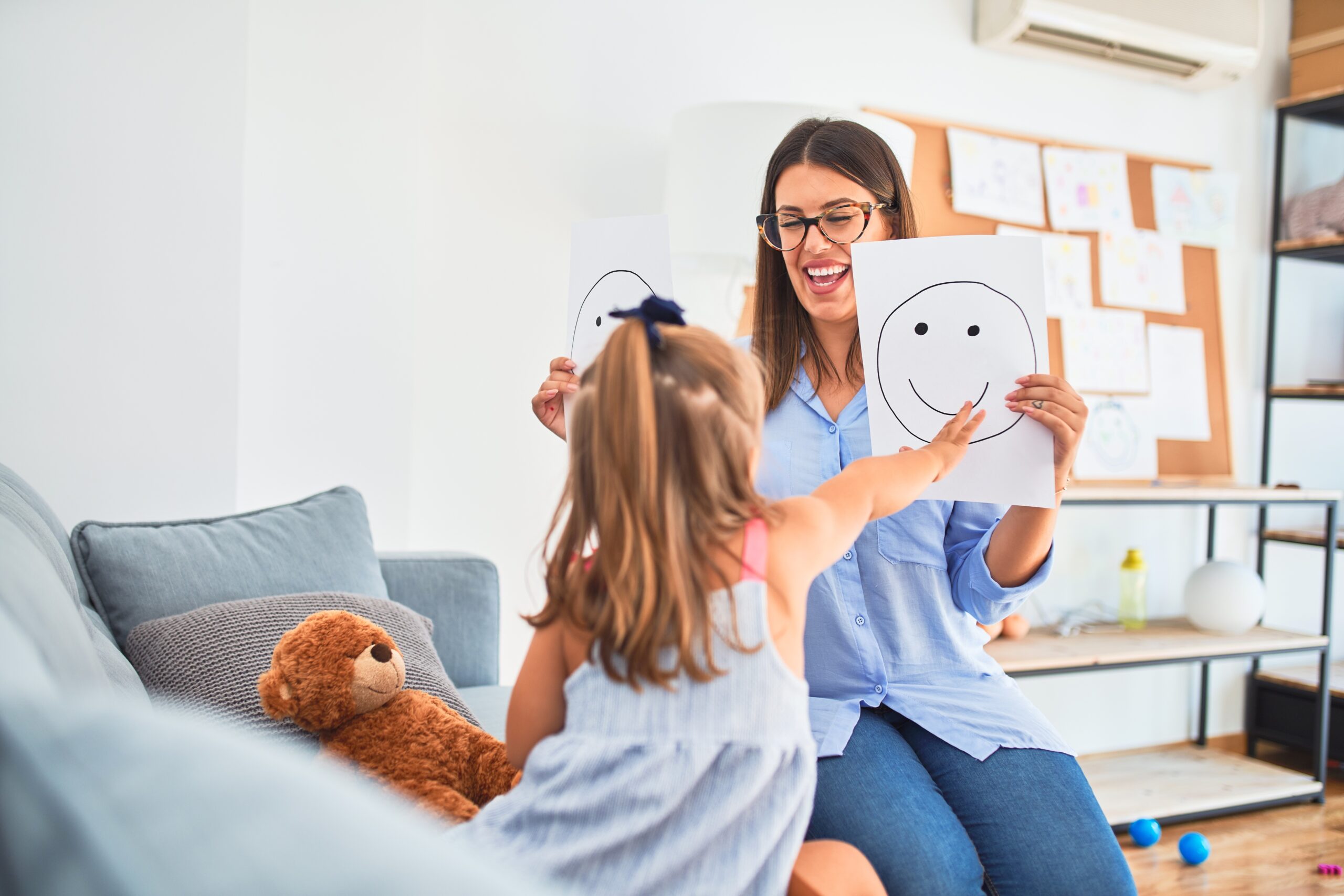 Young therapist woman speaking and treating child, counselor and behaviour correction at pedagogue payroom showing happy and sad faces